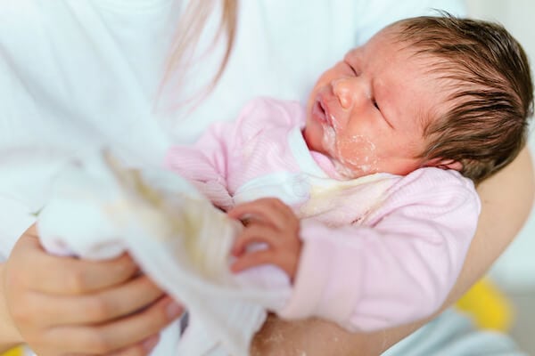 young baby wearing a pink shirt in mothers arms. Mild around mouth because they have spit up after feeding
