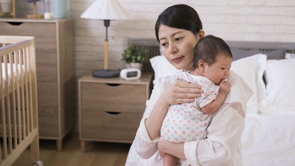 Woman holding her baby on her shoulder while sitting on a bed. Baby is awake, being burped after feeding