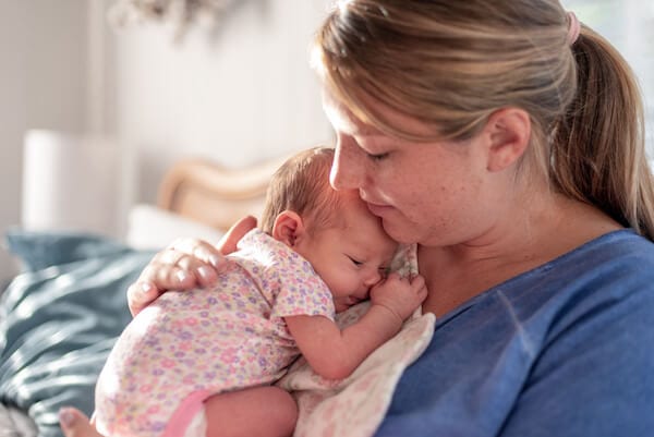 young mother holding her baby upright against her chest after feeding. Baby is asleep and content, mother is gently patting her back