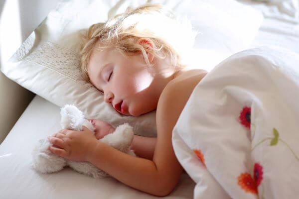 a 2-year-old child sleeping in their bed holding on to a bunny toy