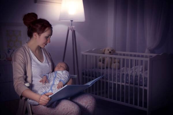 mother reading her newborn a book while sitting in a chair in a dark, quiet room