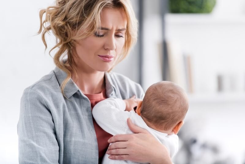 exhausted mother with a sad look on her face holding her baby who is going through a sleep regression and not sleeping well