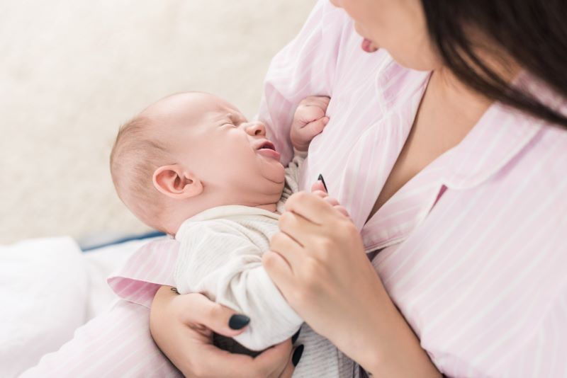 mother cradling her crying baby in her arms, trying to help her baby sleep while experiencing a regression