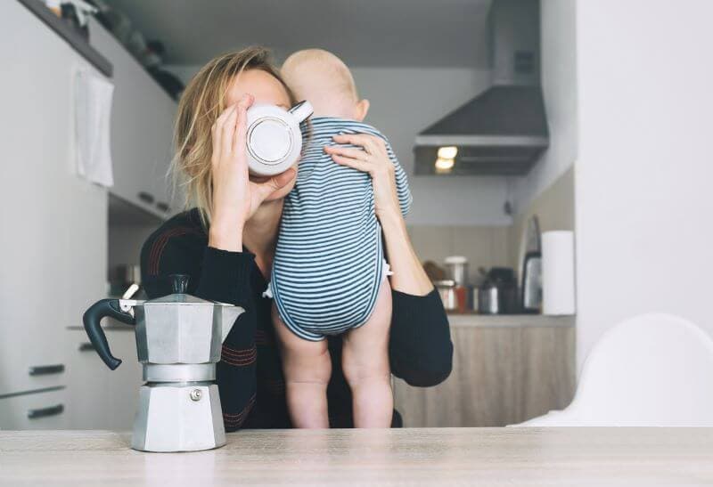 mother holding baby on her shoulder while drinking her coffee quickly. Can't put baby down even for a second to drink her coffee because baby is experiencing separation anxiety.