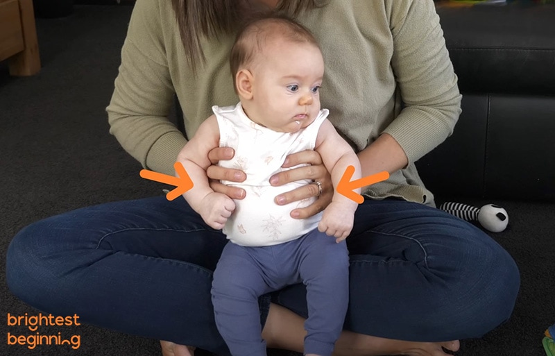 child sitting in mothers lap wearing a white shirt and blue pants. Mother supporter her by holding under her armpits on both sides