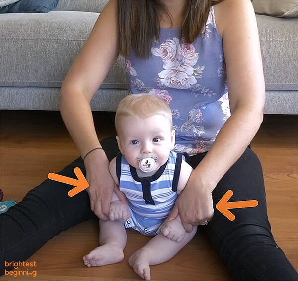 young baby seated between mothers legs facing forwards with pacifier in his mouth
