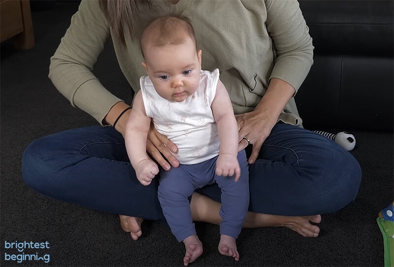 baby sitting on mothers lap with mother supporting her by holding her hips. Baby is slumping to the right because she needs more support